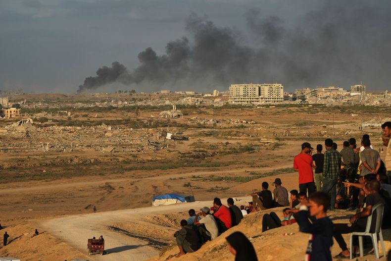 Palestinos desplazados observan cómo se eleva el humo por los ataques del ejército israelí mientras se reúnen en la carretera costera cerca de Wadi Gaza, en el centro de la Franja de Gaza, el jueves 9 de octubre de 2025. (AP Foto/Abdel Kareem Hana)