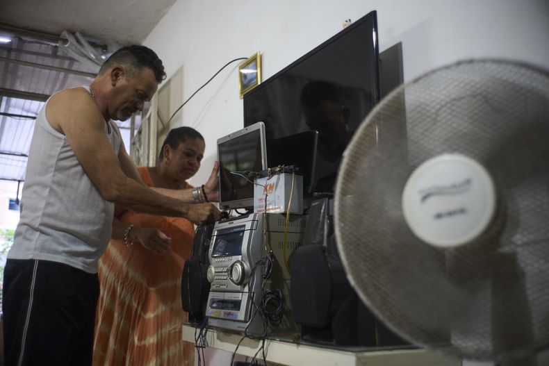 El matrimonio de Ángel Rodríguez y Marylin Álvarez instalan una batería de una motocicleta para conectar la pantalla de una laptop vieja y ver la televisión, como parte de sus preparativos ante los apagones en el barrio de Bahía de La Habana, Cuba, el lunes 26 de mayo de 2025. (AP Foto/Ramón Espinosa)