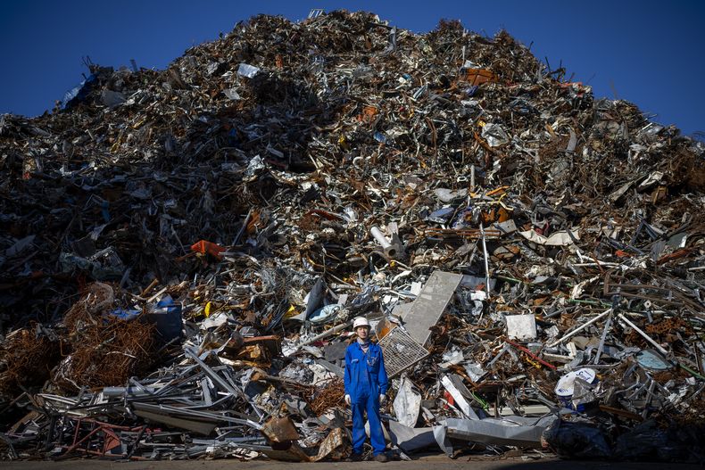 Ma Aijun, de 45 años, de China, posa junto a una montaña de chatarra descargada del buque mercante chino en el que trabaja, en el puerto de Barcelona, España, el viernes 27 de septiembre de 2024. (AP Foto/Emilio Morenatti)