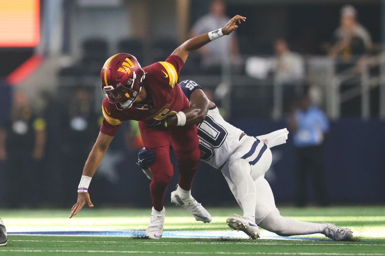 Jayden Daniels, izquierda, es derribado por Shemar James, linebacker de los Cowbous de Dallas, después de provocar un balón suelto durante la segunda mitad del partido de la NFL del domingo 19 de octubre de 2025, en Arlington, Texas. (AP Foto/Gareth Patterson)