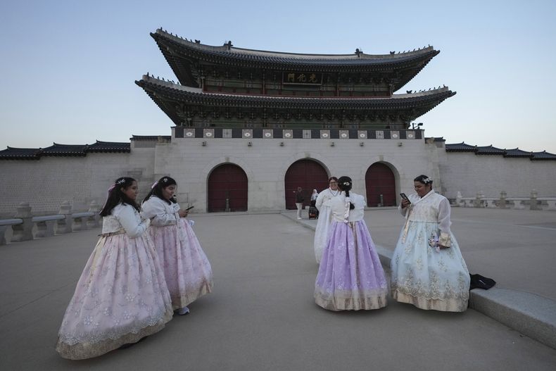 La estadounidense Jessica Hernandez, tercera por la derecha, toma una foto cerca del Gwanghwamun, la puerta principal del palacio Gyeongbok del siglo XIV, uno de los hitos más conocidos de Corea del Sur, en Seúl, Corea del Sur, el miércoles 4 de diciembre de 2024. (AP Foto/Lee Jin-man)