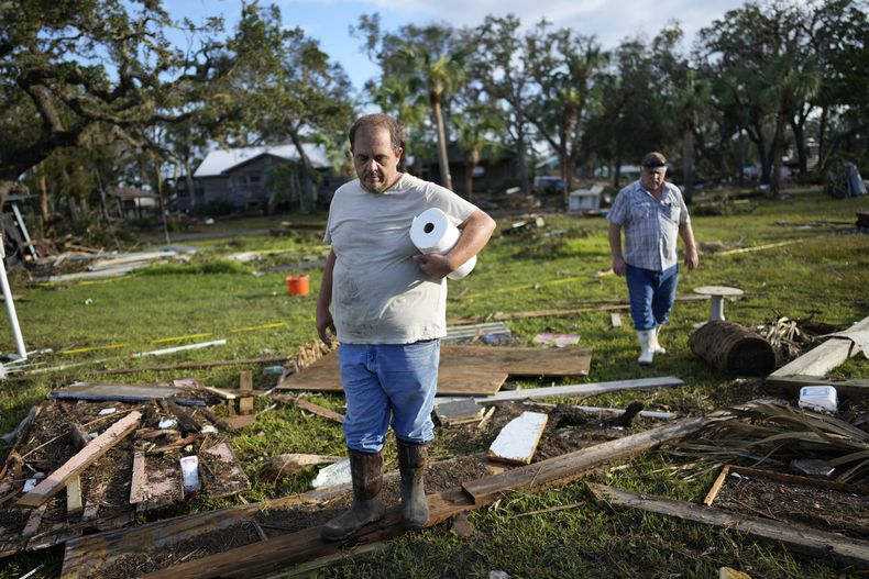 Buddy Ellison (izquierda) y su padre Dan buscan entre los restos esparcidos por su propiedad en Horseshoe Beach, Florida, el 31 de agosto de 2023, un día después del paso del huracán Idalia. (AP Foto/Rebecca Blackwell)