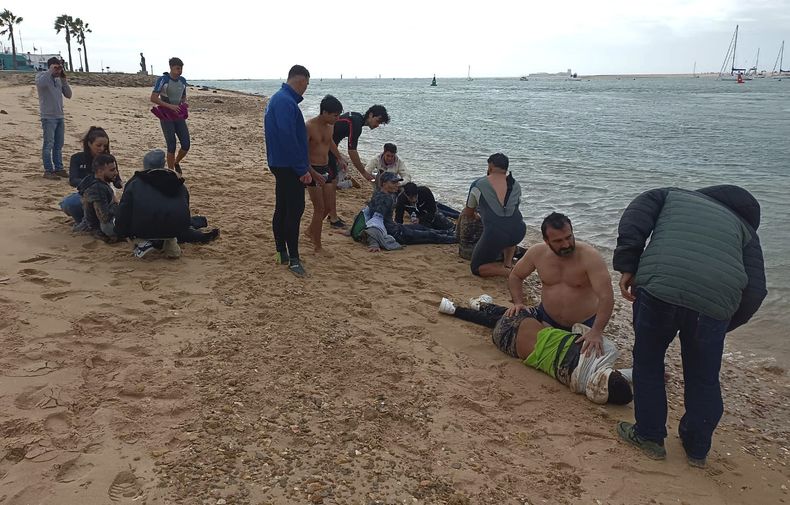 Gente local rescata a migrantes en una playa cerca de Cádiz, España, jueves 30 de noviembre de 2023. Cuatro migrantes murieron a metros de una playa en el sur de España después de ser forzados a bajar del bote en que viajaban, dijeron funcionarios el jueves. La oficina de prensa del gobierno en Cádiz dijo que 31 personas en el bote, incluidos seis menores, sobrevivieron al incidente del miércoles por la tarde y cuatro quedaron hospitalizadas. (AP Foto/Jorge González Casares)