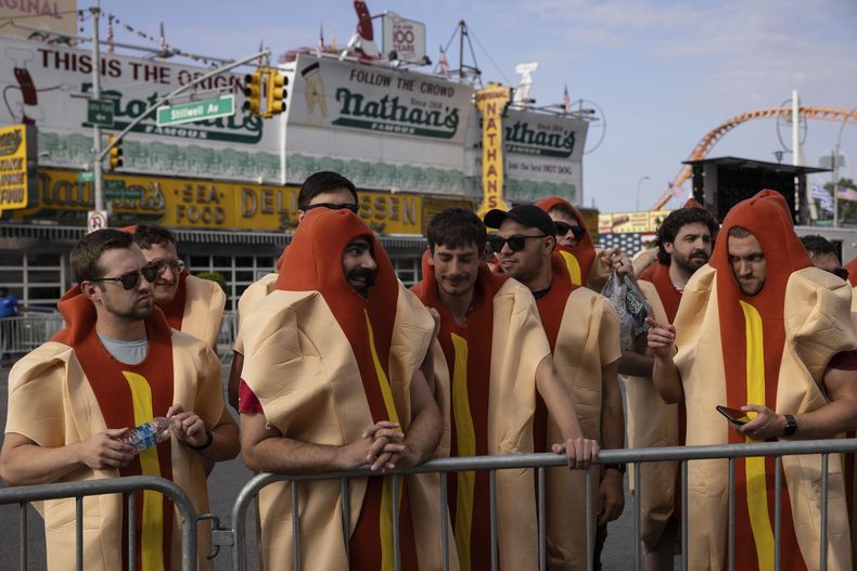 Personas disfrazadas de hot dogs se reúnen antes de que comience el famoso concurso de comer perros calientes organizado por Nathans, el martes 4 de julio de 2023, en Coney Island, Nueva York. (AP Foto/Yuki Iwamura)
