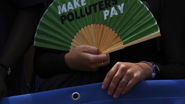 Un activista con un abanico que dice “Que los contaminadores paguen”, en una protesta frente a la sede la Corte Internacional de Justicia en La Haya, Holanda, el 23 de julio del 2025. (AP foto/Peter Dejong)