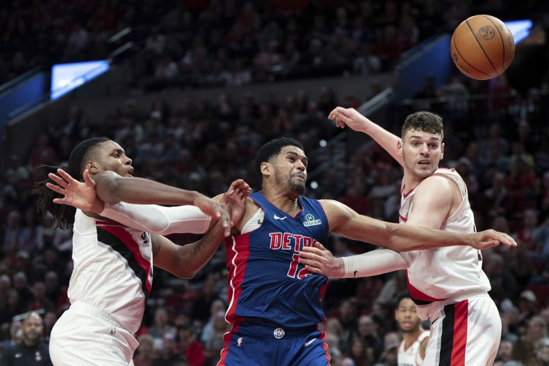 Jabari Walker, izquierda, y Donovan Clingan, derecha, de los Trail Blazers de Portland, deffienden mientras Tobias Harris (12), de los Pistons de Detroit, intenta ir por el balón durante la segunda mitad del juego de baloncesto de la NBA, el domingo 9 de marzo de 2025, en Portland, Oregon. (AP Foto/Jenny Kane)