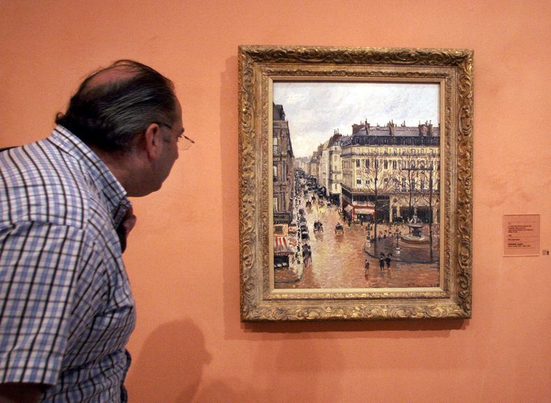 ARCHIVO - Un visitante observa el cuadro impresionista titulado Rue St.-Honore, Apres-Midi, Effet de Pluie (Calle Saint-Honoré por la tarde, efecto de lluvia) pintado en 1897 por Camille Pissarro, expuesto en el Museo Thyssen-Bornemisza el 12 de mayo de 2005, en Madrid. (AP Photo/Mariana Eliano, File)