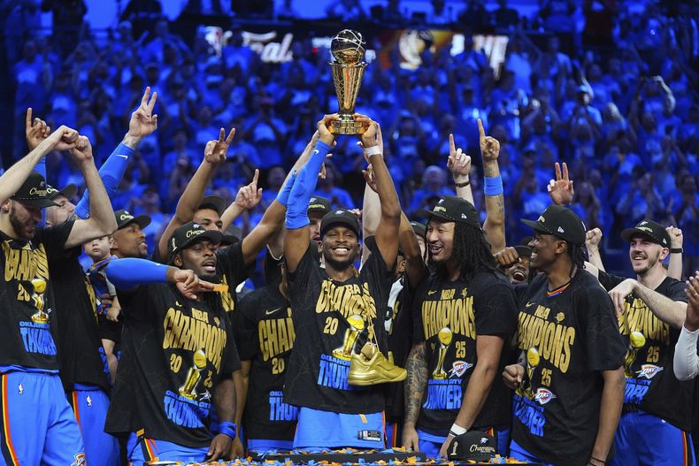 Shai Gilgeous-Alexander, centro, del Thunder de Oklahoma City, alza el trofeo de que proclama campeón de la NBA a su equipo y el del Jugador Más Valioso, mientras sus compañeros de equipo celebran el campeonato de la NBA al ganar el séptimo y decisivo juego de las Finales de la NBA a los Pacers de Indiana, el domingo 22 de junio de 2025, en Oklahoma City. (AP Foto/Julio Cortez)