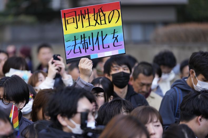Un defensor de la comunidad LGBTQ+ muestra un cartel con la frase Legalicen el matrimonio entre personas del mismo sexo, mientras demandantes hablan con reporteros ante un tribunal tras una sentencia acerca de los derechos maritales de la comunidad, en Tokio, el 14 de marzo de 2024. (AP Foto/Hiro Komae)