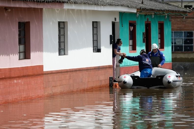 Trabajadores de la Cruz Roja Colombiana entregan el desayuno a una mujer dentro de una casa que se inundó luego de que el río Botello se desbordara debido a las fuertes lluvias en Facatativa, Colombia, el viernes 20 de marzo de 2026. (Foto AP/Fernando Vergara)