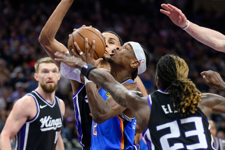 Shai Gilgeous-Alexander, centro, del Thunder de Oklahoma City, ataca el aro superando a Domantas Sabonis, izquierda, Keegan Murray y Keon Ellis (23) durante la segunda mitad del juego de baoncesto de la NBA, en Sacramento, California, el martes 25 de marzo de 2025. (AP Foto/Randall Benton)