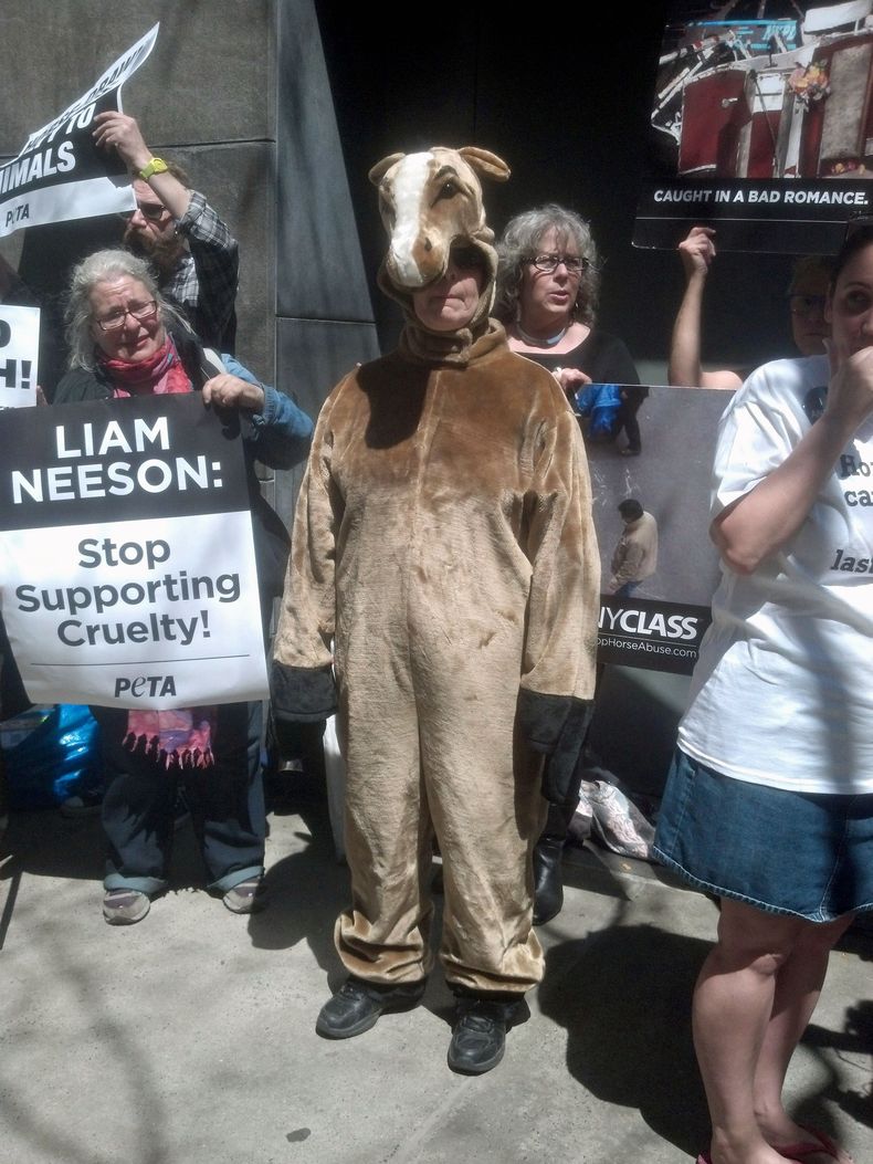 Disfrazada de caballo, Lisa Jablow, al centro, miembro de la organizaci&oacute;n NYCLASS que se opone al uso de carruajes de caballos en Nueva York, se suma a otros activistas frente a la residencia del actor Liam Neeson el s&aacute;bado 19 de abril del 2