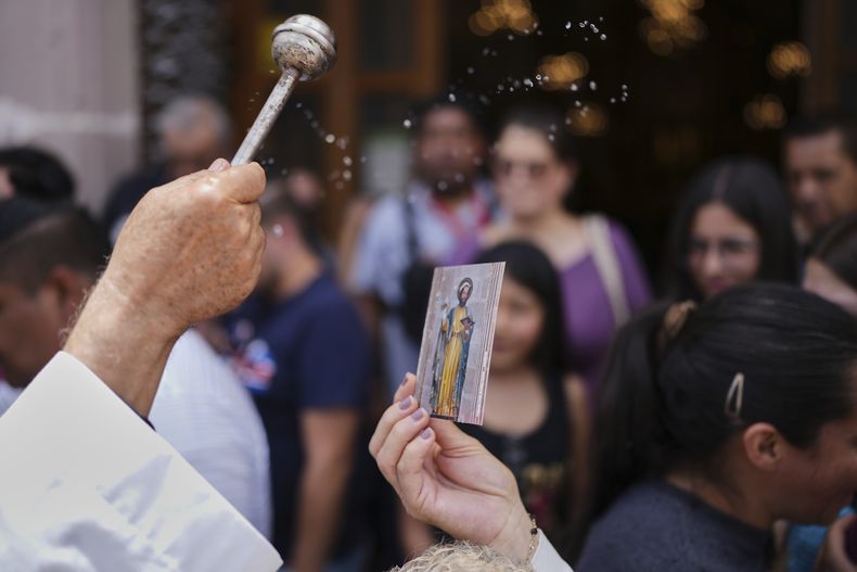 Un sacerdote rocía agua bendita sobre una estampa de San Marcos durante la Feria de San Marcos, un evento de un mes en honor al santo, afuera de la Iglesia de San Marcos en Aguascalientes, México, el viernes 25 de abril de 2025. (AP Foto/Eduardo Verdugo)