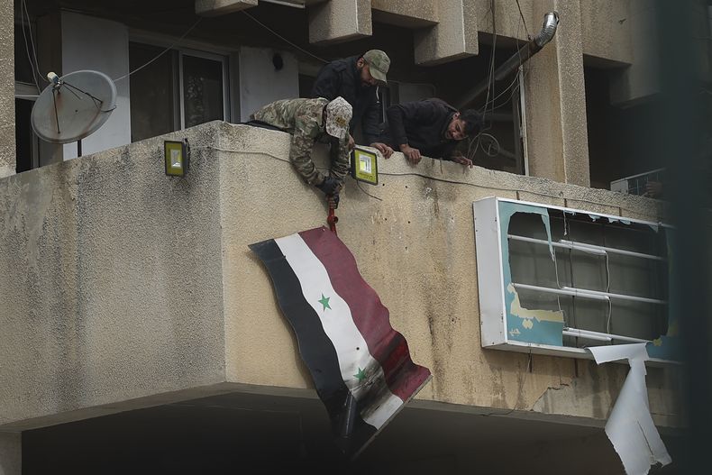 Combatientes de oposición sirios retiran una bandera del gobierno sirio de un edificio oficial en Salamiyah, al este de Hama, Siria, el sábado 7 de diciembre de 2024. (AP Foto/Ghaith Alsayed)