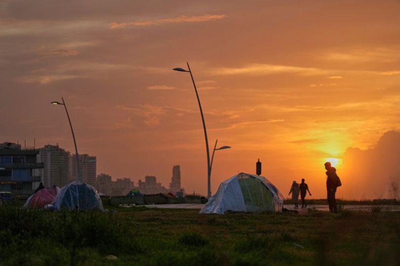 Gente pasa junto a tiendas que cobijan a personas desplazadas por ataques aéreos israelíes en un espacio público junto al paseo marítimo de Beirut, en Líbano, el domingo 15 de marzo de 2026. (AP Foto/Hassan Ammar)