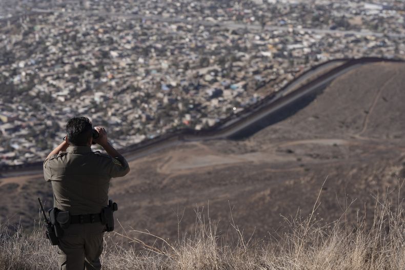 Un agente de la Patrulla Fronteriza usa binoculares para examinar dos muros fronterizos que separan a México de Estados Unidos, el jueves 23 de enero de 2025, en San Diego. (AP Foto/Gregory Bull)