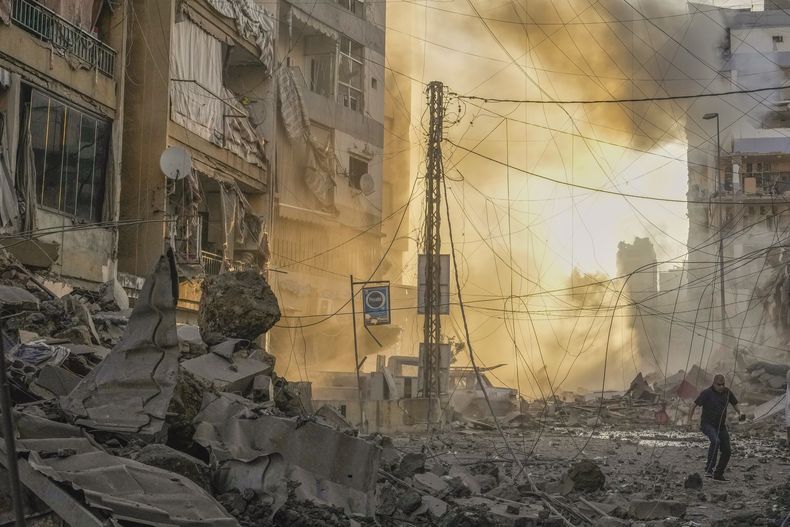 Un hombre corre a ponerse a cubierto mientras de fondo se puede ver el humo provocado por un ataque aéreo israelí en Dahiyeh, Beirut, Líbano, el 4 de octubre de 2024. (AP Foto/Hassan Ammar)