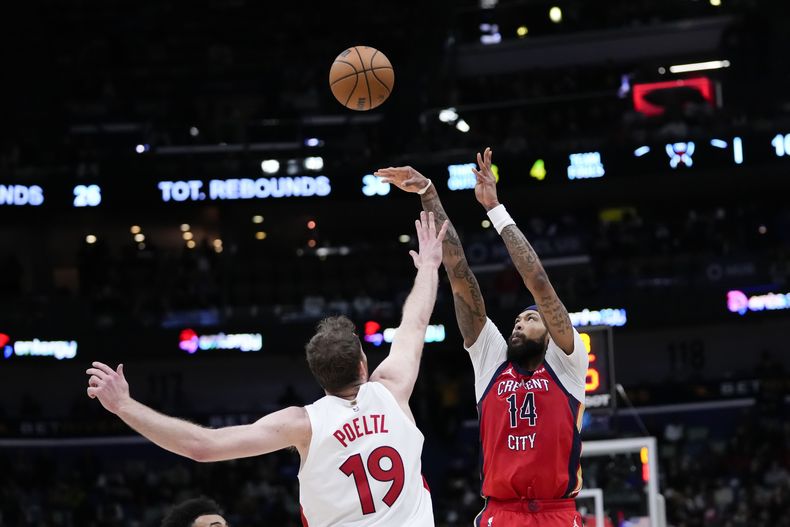 Brandon Ingram (14), de los Pelicans de Nueva Orleans, lanza un tiro de tres puntos con la presión de Jakob Poeltl (19), de los Raptors de Toronto, en la segunda mitad del juego de baloncesto de la NBA, en Nueva Orleans, el lunes 5 de febrero de 2024. (AP Foto/Gerald Herbert)