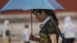 ARCHIVO - Una mujer con un ventilador eléctrico en el cuello y un paraguas visita la Ciudad Prohibida en un día caluroso en Beijing, el 7 de julio de 2023. Nueve personas estaban desaparecidas en el centro de China después de un deslave provocado por aguaceros, en medio de inundaciones y olas de calor que castigaban buena parte del país, según dijeron las autoridades el domingo. (AP Foto/Andy Wong, Archivo)