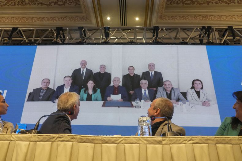 Miembros de la delegación del prokurdo Partido del Pueblo por la Igualdad y la Democracia (DEM) difunden una declaración del encarcelado líder del grupo rebelde Partido de los Trabajadores de Kurdistán (PKK), Abdullah Ocalan, centro en la foto del fondo, en Estambul, Turquía, el 27 de febrero del 2025. (AP foto/Khalil Hamra)