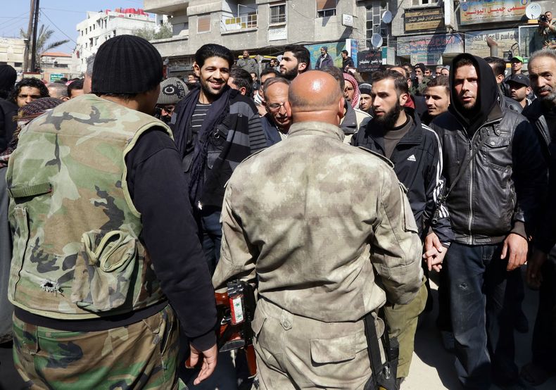 Rebeldes sirios, al fondo, conversan con fuerzas del gobierno sirio, en primer plano, tras de que las partes concertaran un acuerdo de reconciliaci&oacute;n en el poblado de Babila, al sureste de Damasco, Siria, el lunes 17 de febrero de 2014. El domingo