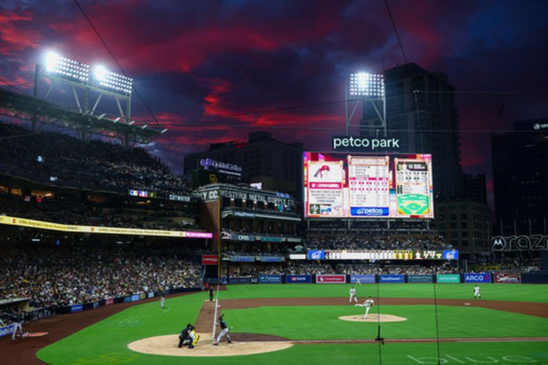 El abridor de los Padres de San Diego, Walker Buehler (centro), realiza un lanzamiento hacia Corbin Carroll, de los Diamondbacks de Arizona (tercero desde la izquierda), durante la cuarta entrada de un partido de béisbol el sábado 26 de septiembre de 2026 en San Diego. (Foto AP/Karl Anderson)