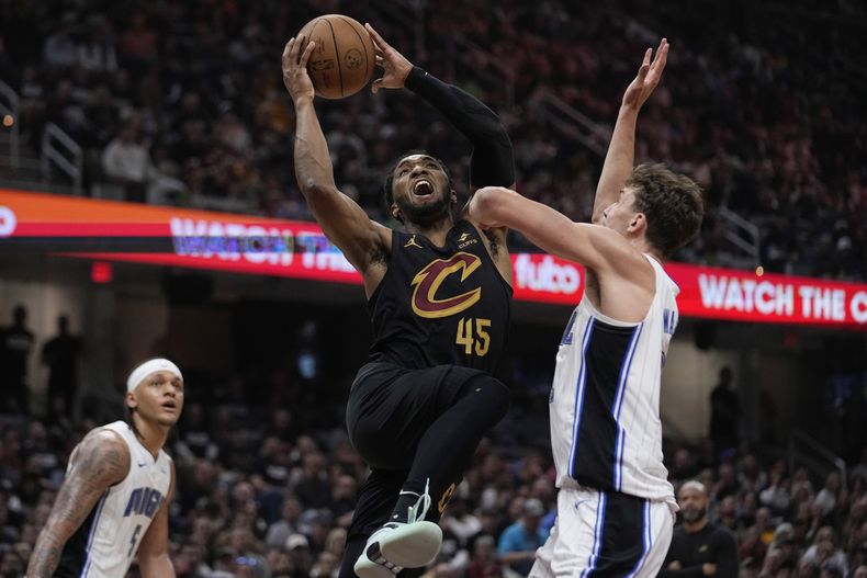 El armador de los Cavaliers de Cleveland Donovan Mitchell (45) lanza entre el escolta del Orlando Magic Paolo Banchero (5) y el alero Franz Wagner (derecha), en la primera mitad del Juego 7 de la primera ronda de playoffs de la NBA, el domingo 5 de mayo de 2024, en Cleveland. (AP Foto/Sue Ogrocki)