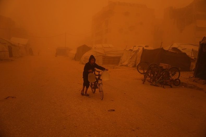 Un chico lleva una bicicleta con bidones de agua a través de una tormenta de arena en Jan Yunis, en el sur de la Franja de Gaza, el sábado 14 de marzo de 2026. (AP Foto/Abdel Kareem Hana)