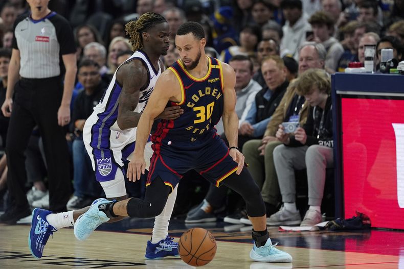 El escolta de los Warriors de Golden State, Stephen Curry (30), mueve el balón mientras es defendido por el escolta de los Kings de Sacramento, Keon Ellis, durante la primera mitad de un partido de baloncesto de la NBA, el jueves 13 de marzo de 2025, en San Francisco. (AP Foto/Godofredo A. Vásquez)