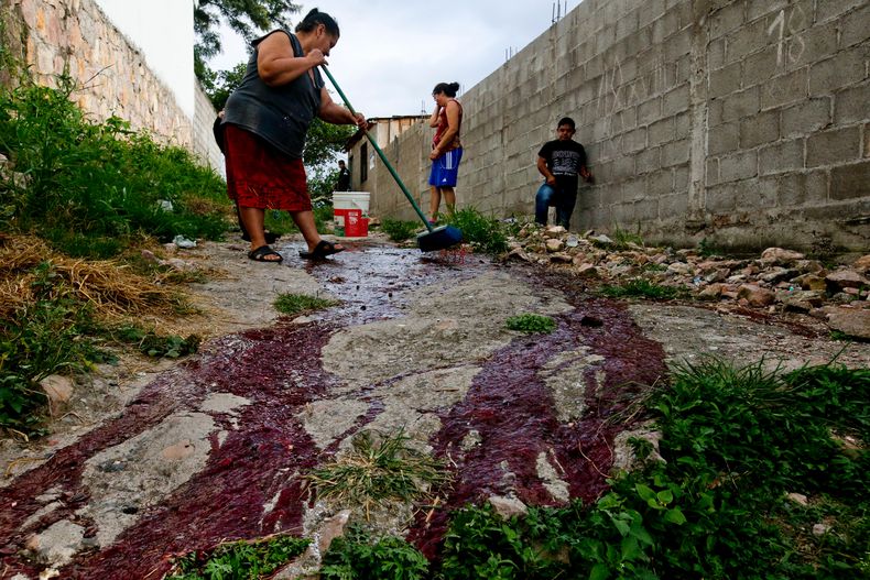 Familiares de Ronald Blanco limpian su sangre del callejón en el vecindario Japón, donde fue asesinado y donde opera la pandilla Barrio 18, en Tegucigalpa, Honduras, el 2 de agosto de 2018. (AP Foto/Esteban Felix)