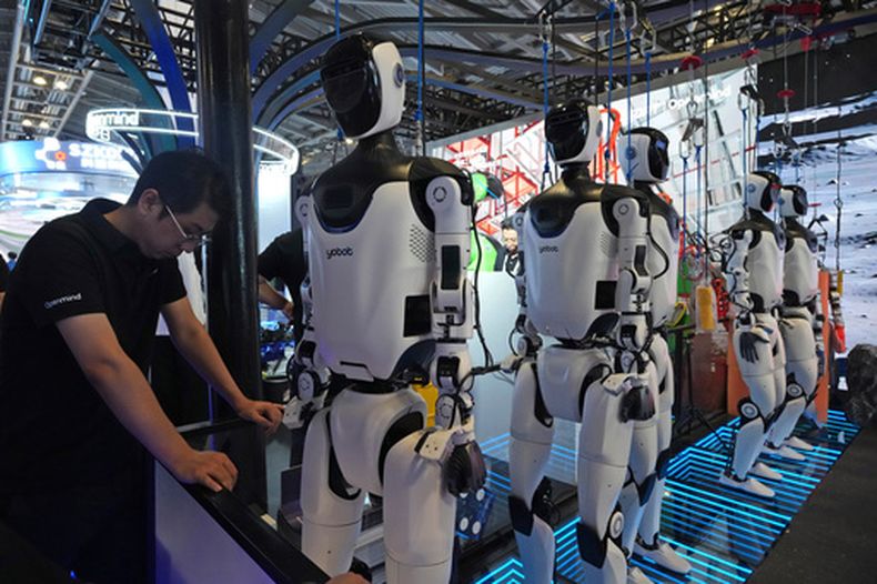 ARCHIVO - Un trabajador se ve junto a una fila de robots humanoides en la conferencia World AI Conference en Shanghái, el viernes 17 de julio de 17, 2026. (AP Foto/Ng Han Guan, archivo)