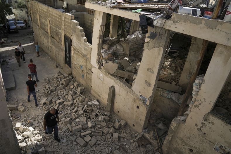 Palestinos pasan junto a una casa dañada en el campamento de refugiados de Yenín, en Cisjordania, el miércoles 5 de julio de 2023, después de que el ejército israelí retirase a sus tropas de ese bastión de milicianos. (AP Foto/Nasser Nasser)