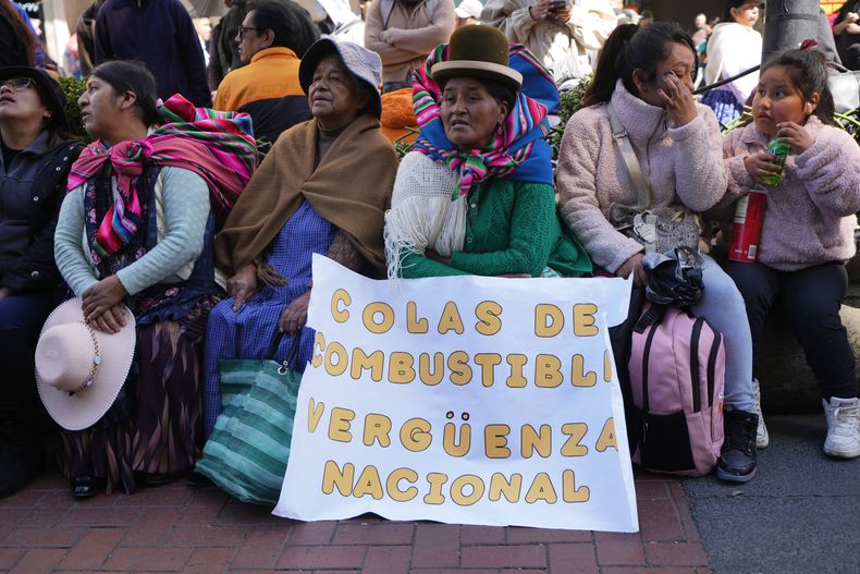 Comerciantes descansan después de manifestarse en contra de la crisis económica ante un cartel que dice Colas de combustible, vergüenza nacional en La Paz, Bolivia, Miércoles 21 de mayo de 2025. (AP Foto/Juan Karita)