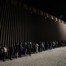 Un grupo de personas hacen fila junto al muro fronterizo mientras esperan para solicitar asilo tras cruzar al frontera desde México, el 11 de julio de 2023, cerca de Yuma, Arizona. El repunte en la inmigración ha sido posible por el descubrimiento este año de una nueva a través de Nicaragua, donde la laxitud de los requisitos de entrada permite a los mauritanos y a otros extranjeros adquirir una visa de bajo costo sin necesidad de demostrar que van a continuar su viaje. (AP Foto/Gregory Bull)