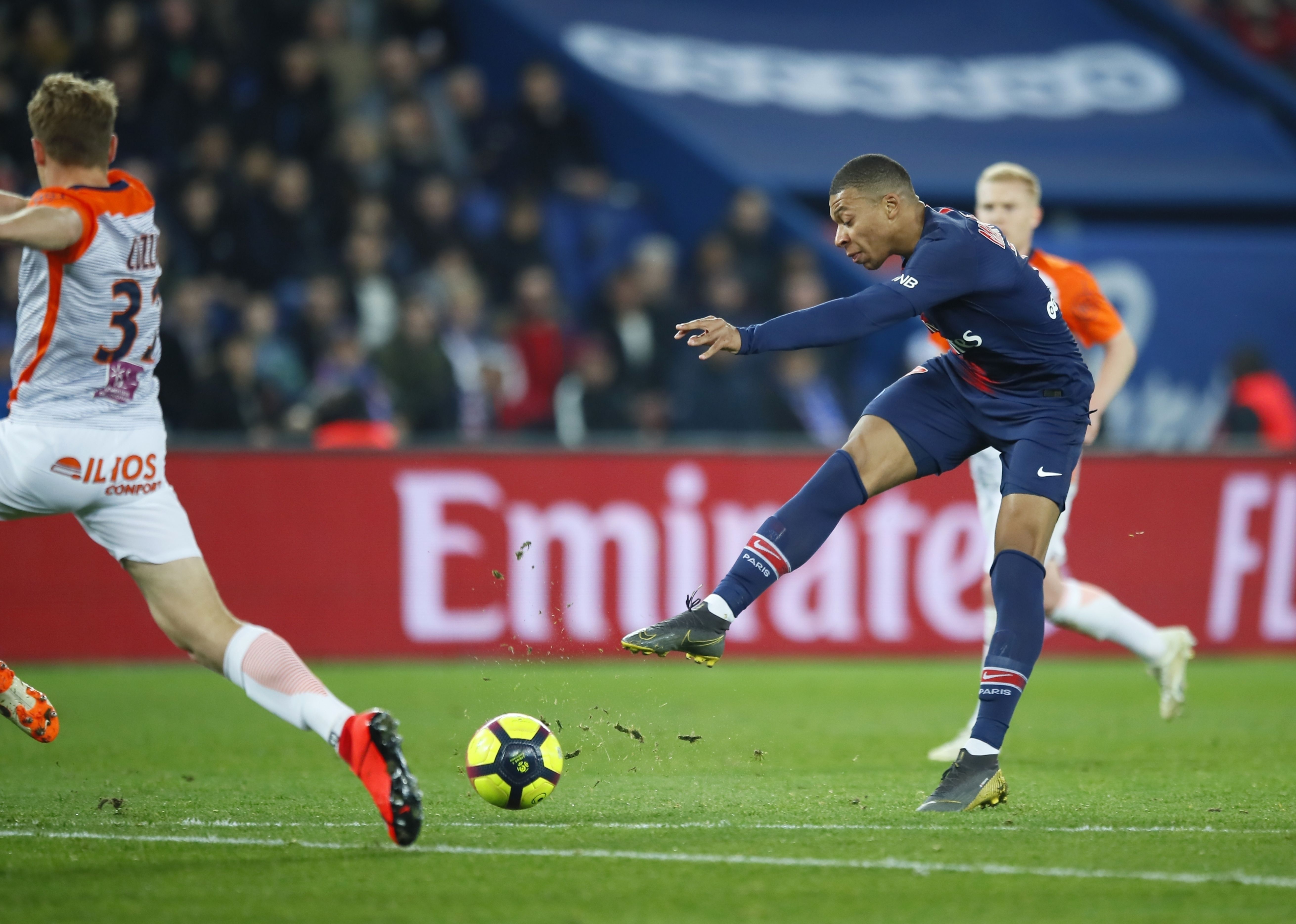  Kylian Mbappe in a blue and red jersey is about to kick the ball into the goal while playing in a Champions League match.