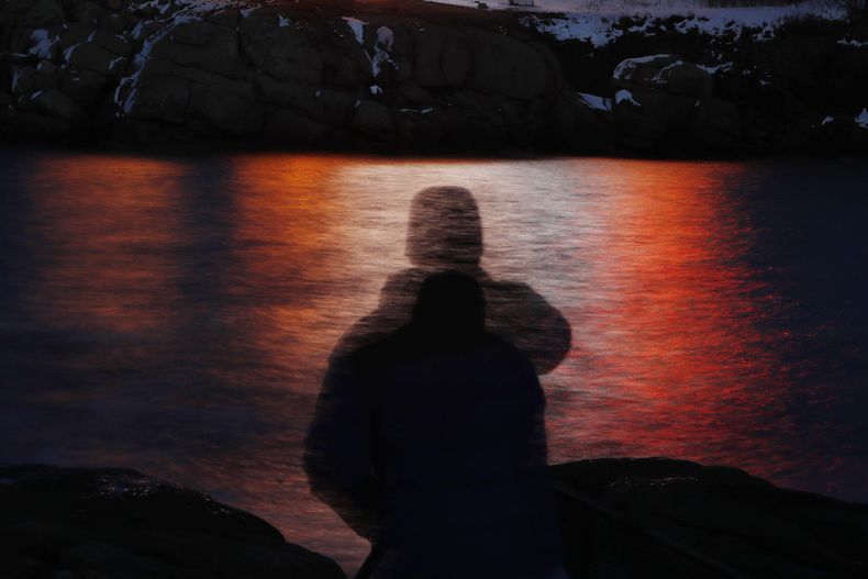 ARCHIVO - En esta foto, tomada con un tiempo de exposición largo, la silueta de un hombre aparece frente a las luces reflejadas en las aguas de Cape Neddick en Maine , el 11 de diciembre de 2017. (AP Foto/Robert F. Bukaty, Archivo)