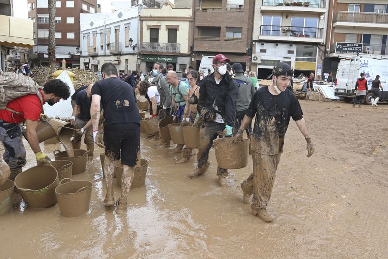 Voluntarios cargan cubetas con lodo tras las inundaciones en Paiporta, cerca de Valencia, España, el 3 de noviembre de 2024. (AP Foto/Hugo Torres)