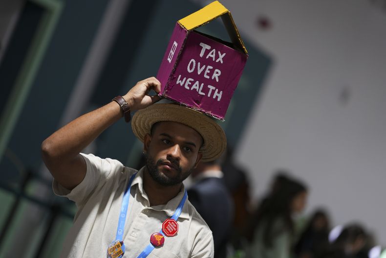 Una persona camina con un objeto con forma de casa sobre la cabeza, con la frase impuesto sobre salud, en la cumbre climática de Naciones Unidas, o COP29, el 16 de noviembre de 2024, en Bakú, Azerbaiyán. (AP Foto/Peter Dejong)
