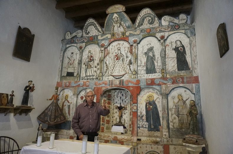 El maestro santero Félix López, un artista entrenado en la tradición de escultura y pintura religiosa de Nuevo México, que se remonta siglos atrás, habla durante una entrevista el domingo 16 de abril de 2023 frente a un retablo de la década de 1810 que él limpió y preservó, en la misión del Santo Rosario en Truchas, Nuevo México. (AP Foto/Giovanna DellOrto)