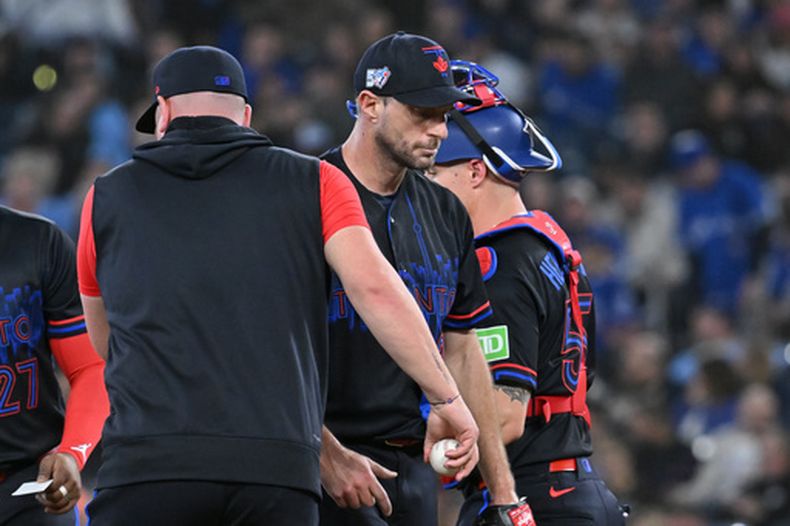 Max Scherzer, centro, lanzador de los Azulejos de Toronto, es retirado en la tercera entrada del juego de béisbol de Grandes Ligas contra los Guardianes de Cleveland por el mánager John Schneider, el viernes 24 de abril de 2026, en Toronto. (Jon Blacker/The Canadian Press via AP)