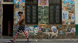 Una mujer que lleva unos pantalones con motivos de la bandera estadounidense pasa junto a un edificio que alberga una instalación artística sobre la Revolución Cubana, en la que se exhiben fotografías del expresidente cubano Raúl Castro y del expresidente venezolano Nicolás Maduro, en La Habana, Cuba, el martes 19 de mayo de 2026. (AP Foto/Ramón Espinosa)