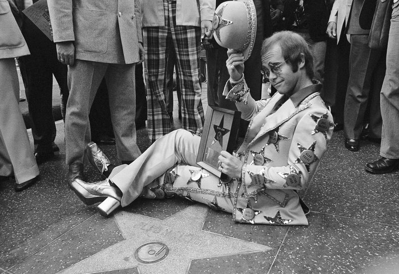 ARCHIVO - Elton John posa junto a su estrella en el Paseo de la Fama de Los Ángeles el 23 de octubre de 1975. (Foto AP/Jeff Robbins, archivo)