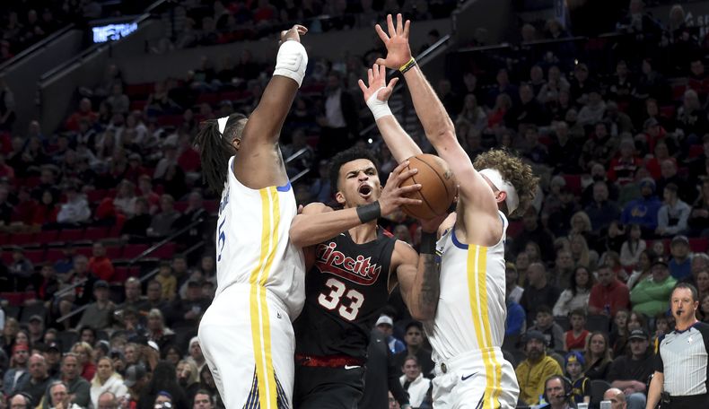 Toumani Camara (33), de los Trail Blazers de Portland, intenta pasar entre Kevon Looney, izquierda, y Brandin Podziemski, derecha, durante la primera mitad del juego de baloncesto de la NBA, el 17 de diciembre de 2023, en Portland. (AP Foto/Steve Dykes)