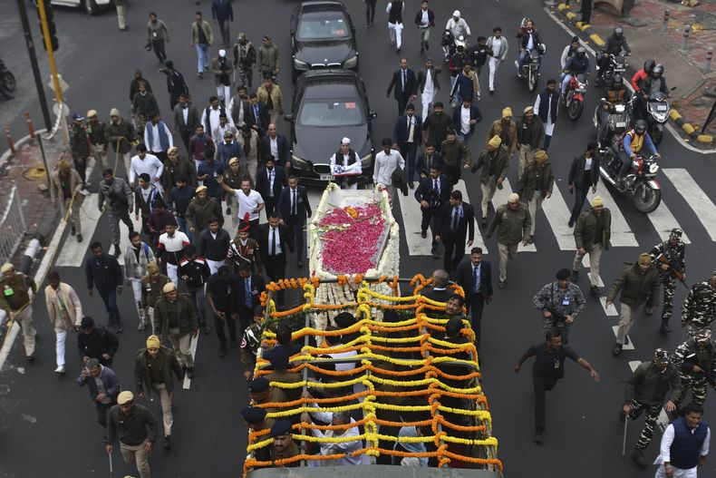 Agentes de seguridad y otras personas caminan junto al vehículo fúnebre que traslada el cuerpo del ex primer ministro de India Manmohan Singh hacia el lugar donde será incinerado, en Nueva Delhi, India, el 28 de diciembre de 2024. (AP Foto)