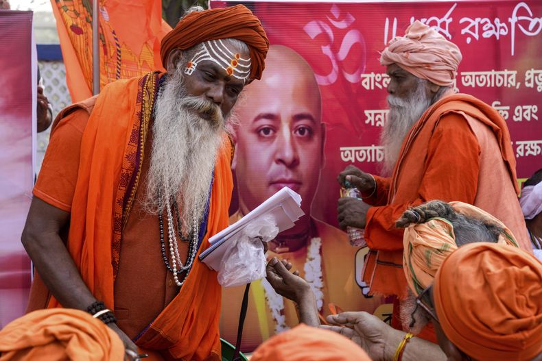 Una sección de monjes hindúes o sadhus asiste a una concentración de protesta en condena de la reciente detención del destacado líder hindú Krishna Das Prabhu (imagen de fondo) y de los supuestos ataques a hindúes en Bangladesh, en Calcuta, India, jueves 5 de diciembre de 2024. (AP foto/Bikas Das)
