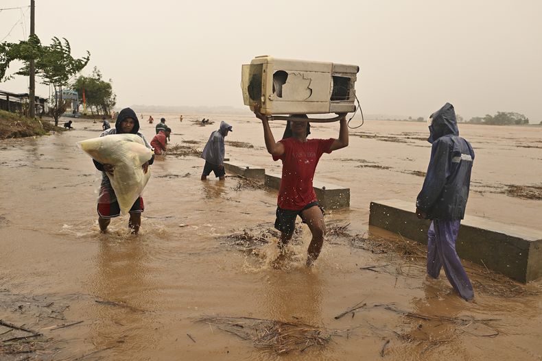 Dos personas cargan sus pertenencias junto a un río crecido tras intensas lluvias causadas por el tifón Toraji, el lunes 11 de noviembre de 2024, en Ciudad Ilagan, provincia de Isabela, en el norte de Filipinas. (AP Foto/Noel Celis)