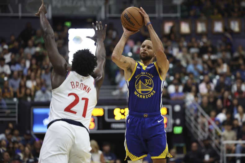 El base de los Warriors de Golden State Stephen Curry lanza el balón sobre Kobe Brown de los Clippers de Los Ángeles en el encuentro de exhibición del sábado 5 de octubre del 2024 en Honolulu. (AP Foto/Marco Garcia)