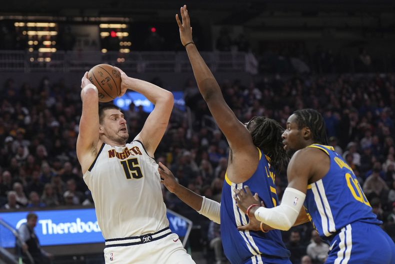 El serbio Nikola Jokic, de los Nuggets de Denver, busca enviar un pase frente a Kevon Looney (centro) y Jonathan Kuminga, de los Warriors de Golden State, el jueves 4 de enero de 2024 (AP Foto/Loren Elliott)