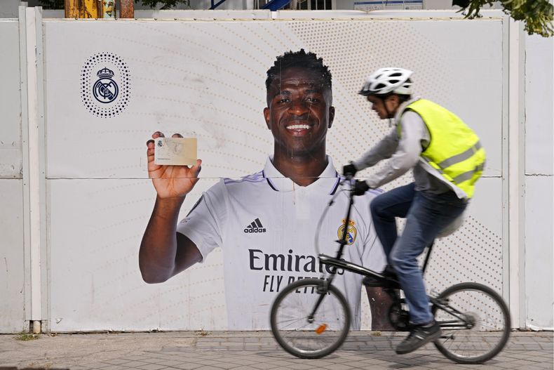 Un ciclista pasa frente a un afiche de Vinicius Junior, el delantero brasileño del Real Madrid, frente al estadio Santiago Bernábeu, el lunes 22 de mayo de 2023 en Madrid. (AP Foto/Paul White)