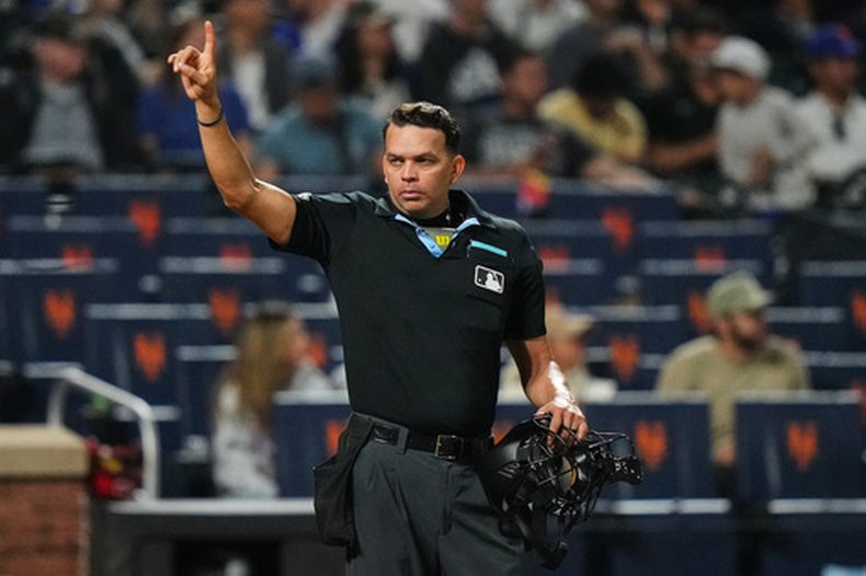 El umpire de home Emil Jiménez hace un gesto a los jugadores durante la octava entrada de un partido de béisbol entre los Mets de Nueva York y los Rojos de Cincinnati, el martes 26 de mayo de 2026, en Nueva York. (Foto AP/Frank Franklin II)